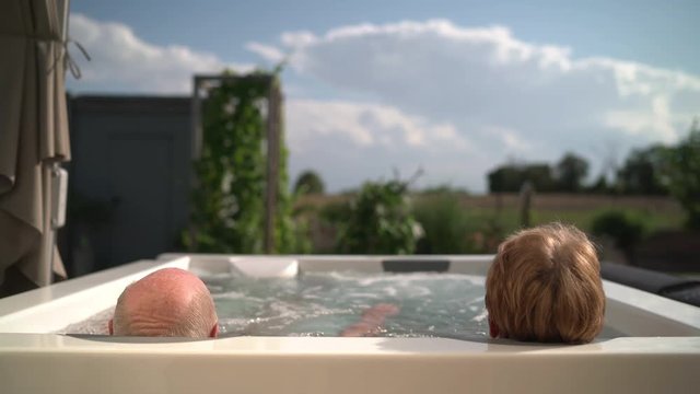 4k video rear view senior couple relaxing in whirlpool outdoors in garden on sunny summer day
