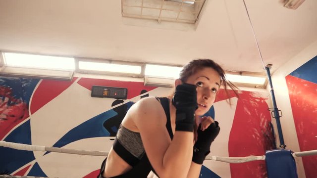 Young female athlete doing shadow boxing exercise in a boxing gym. Low angle view. Slow motion shot.