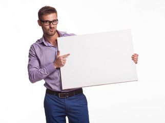 Young jocular man portrait of a confident businessman showing presentation, pointing paper placard gray background. Ideal for banners, registration forms, presentation, landings, presenting concept.