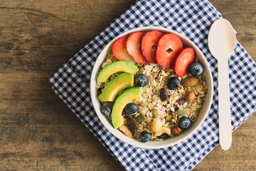 Muesli or granola on white bowl with fresh fruits nuts and cereal. Granola top with blueberries strawberries and avocado served with milk and honey for breakfast.Granola is healthy food for dieting.