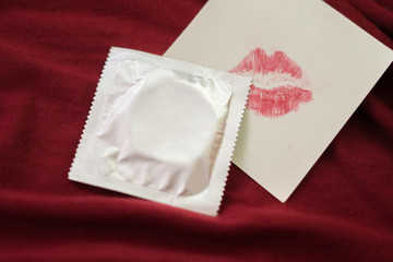 Condom and Lipstick on red bed sheet.