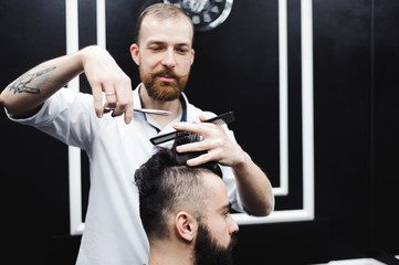 Young handsome barber making haircut of attractive man in barbershop