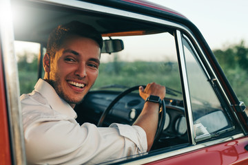 Rear view of handsome happy male driver smiling while sitting in a car with open front window. Smiling Caucasian man drive a car on roadtrip adventure travel.