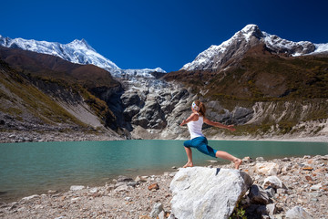 Woman is doing yoga excercises near big lake on the Manaslu circuit trak in Nepala