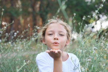 Portrait of a cute little girl sends an air kiss on the nature.