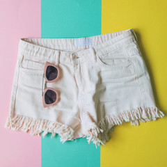 light pink denim shorts with fringe and sunglasses on colorful paper background in style pop art