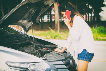 Woman using smartphone at the side of the road with broken car.