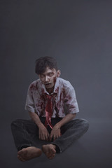 Horrible asian scary zombie man with wounded face sitting