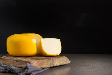 Round gouda cheese. Dark background. - obrazy, fototapety, plakaty