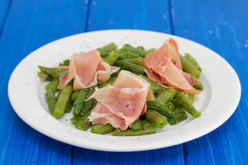 green beans with prosciutto on white plate on wooden background