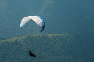 A paraglider flies over a mountain valley on a sunny summer day. Paragliding competitions in the...