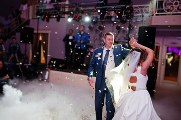 Newly married couple dancing on their wedding party with heavy smoke and multicolored lights on the background.