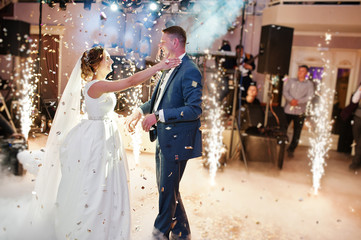 Newly married couple dancing on their wedding party with heavy smoke, multicolored lights and fireworks on the background.