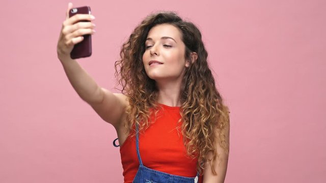 Young happy caucasian woman make selfie by phone isolated over pink background