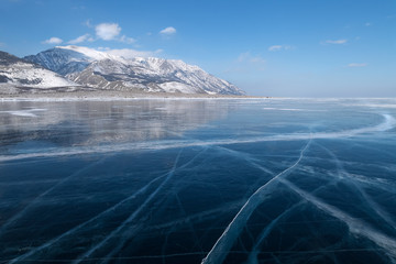 Glossy smooth surface with cracks of frozen blue ice field of lake Baikal, winter landscape