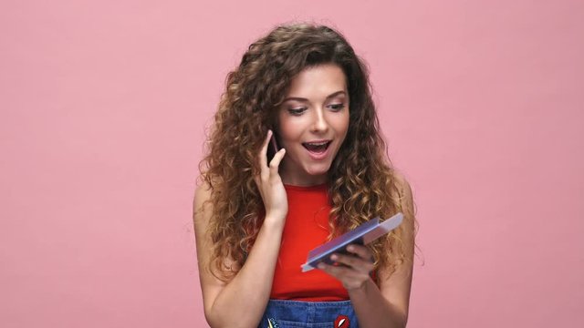 Young happy caucasian lady standing over pink background holding passport and tickets talking by phone