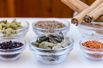 Different kind of indian spices such as cardamom, cumin, curry leaves,  cinnamon in glass bowls. 