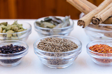 Different kind of indian spices such as cardamom, cumin, curry leaves,  cinnamon in glass bowls. 