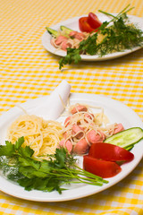 Pasta with sausage and tomatoes with greens on a white plate
