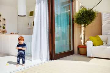 a toddler baby walking on open space kitchen with roof top patio and sliding doors