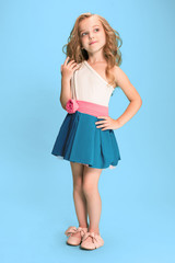 Full length of beautiful little girl in dress standing and posing over blue background