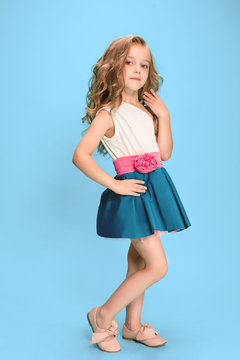 Full length of beautiful little girl in dress standing and posing over blue background
