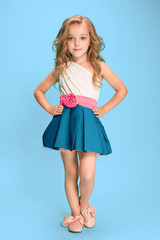 Full length of beautiful little girl in dress standing and posing over blue background