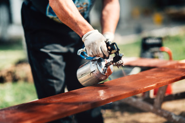 Close-up details of man using spray gun or airbrush for painting  fence. Carpentry details with...