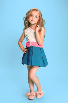 Full length of beautiful little girl in dress standing and posing over blue background