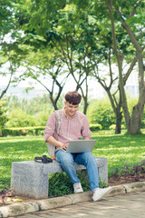 Fototapeta premium Young man sitting on bench in park, reading book, smiling and looking into the camera