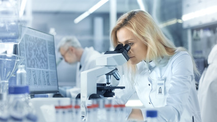 Female Research Scientist Looks at Biological Samples Under Microscope. She and Her Colleagues Work...