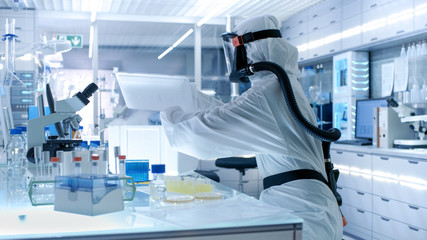 Medical Virology Research Scientist Works in a Hazmat Suit with Mask, She Takes out Test  Tubes from Refrigerator Box. She Works in a Sterile High Tech Laboratory, Research Facility.