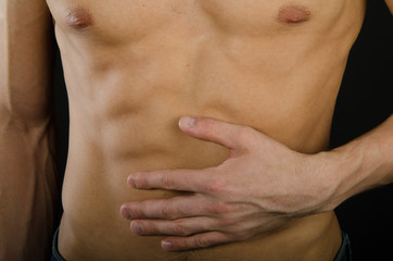 Naklejka premium Abdominal pain. A young man without a shirt. Black background. 