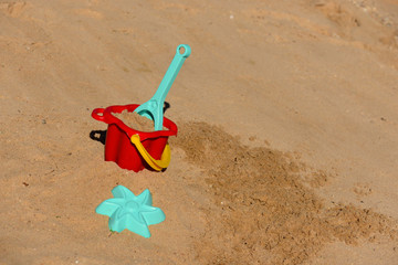 Baby beach toys - bucket, shovel and pask in the sand on a sunny day.