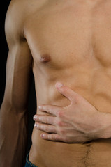 Abdominal pain. A young man without a shirt. Black background. 