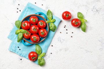 Fresh cherry tomatoes in a bowl, basil leaves and black pepper on stone table, closeup, top view...