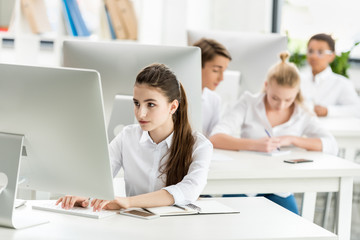 portrait of focused teenage girl in white shirt working on computer while studying in classroom