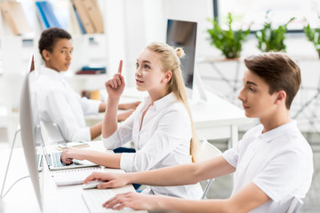 selective focus of teenage girl pointing up while sitting at table with laptop in class