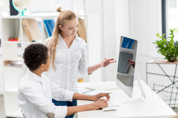 multicultural students discussing task at computer screen in class