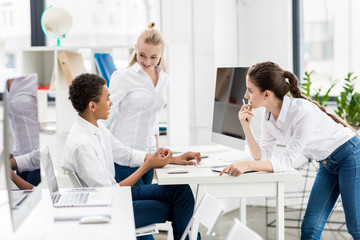 side view of multicultural students in white shirts working on project together in class