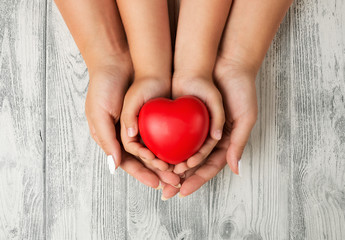 Close up of mother and children hands holding red rubber heart together