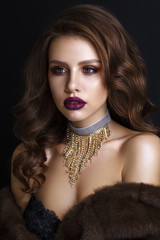 Beautiful young model with evening makeup, perfect skin, wavy long hairstyle in fur cout on black background. Trendy colorful smoky eyes. Purple lips