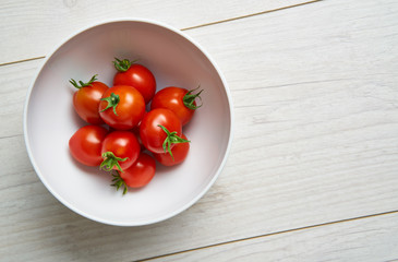 Bright red ripe tomatoes in a white ceramic bowl on a pale wood work surface, worktop in a kitchen.