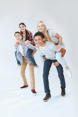 Fototapeta premium happy multicultural boys and girls piggybacking together isolated on white