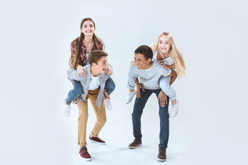 Fototapeta premium happy multicultural boys and girls piggybacking together isolated on white