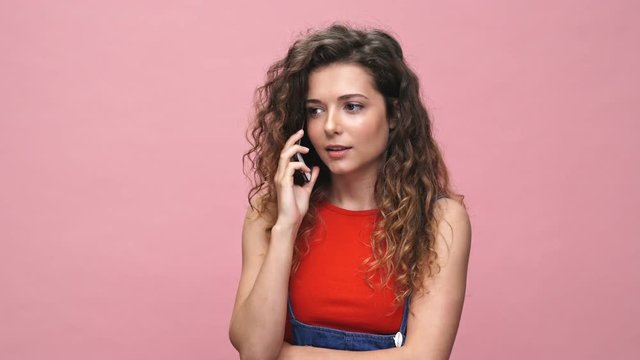Young serious caucasian woman talking with friends by phone isolated over pink background