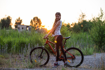 Fototapeta na wymiar Attractive sporty girl with long hair on a bicycle drinking water from the sport bottle on sunset