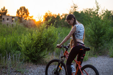 Fototapeta premium Attractive sporty girl with long hair on a bicycle drinking water from the sport bottle on sunset