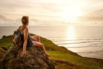 Hiker with backpack enjoying sunset listening to music on peak of mountain. - obrazy, fototapety, plakaty