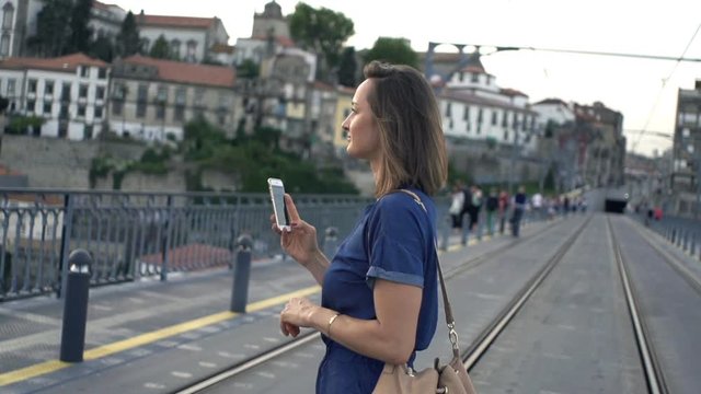 Young woman with smartphone walking on bridge in Porto, Portugal, super slow motion 240fps
